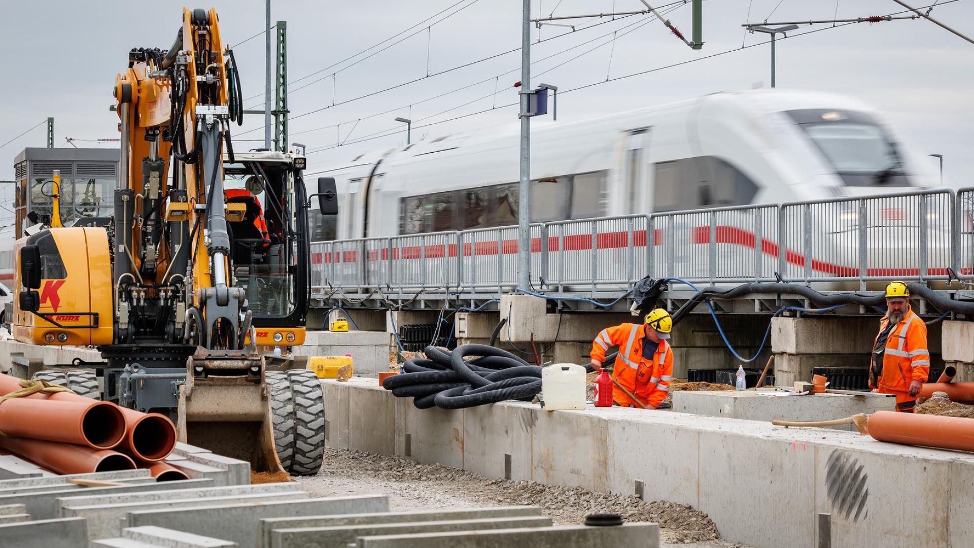 Bauarbeiter arbeiten auf einer Baustelle, im Hintergrund ist ein ICE zu sehen