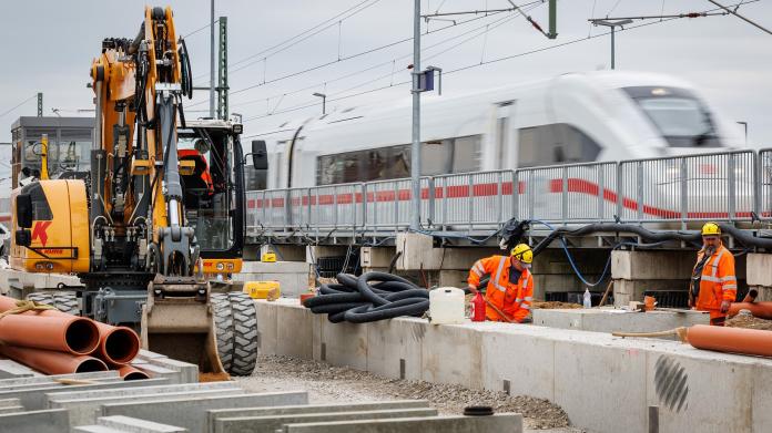 Bauarbeiter arbeiten auf einer Baustelle, im Hintergrund ist ein ICE zu sehen